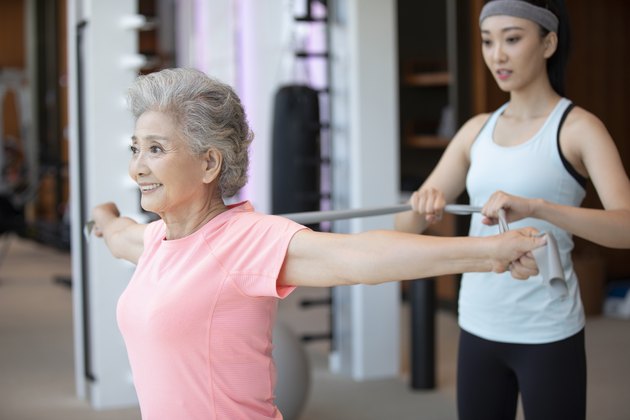 Senior Chinese woman working out with personal trainer at gym