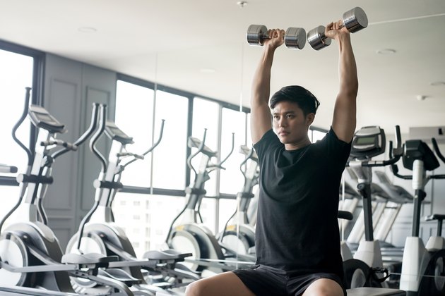 Young man shoulder pressing dumbbells.