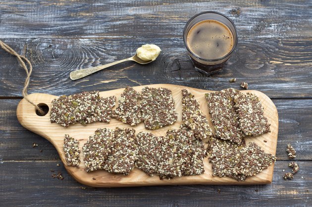 Delicious healthy multigrain gluten-free crackers, ketogenic, from chia seeds, flax, sesame and ground pumpkin seeds and keto coffee in glass with spoon of butter оn wooden table