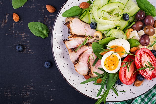 Ketogenic diet. Keto brunch. Boiled egg, pork steak and olives, cucumber, spinach, brie cheese, nuts and tomato. Top view