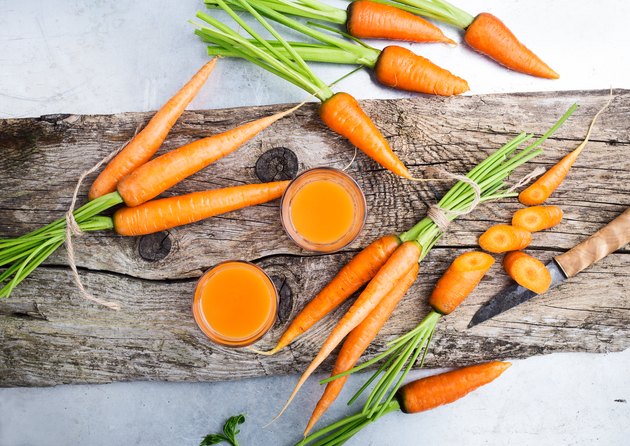Fresh carrot juice and raw organic vegetables over rustic wooden table
