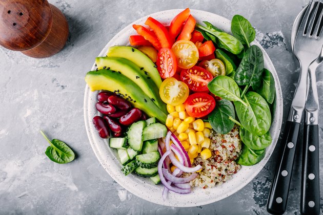 Healthy vegan lunch features immune boosting foods like avocado, quinoa, tomato, cucumber, red beans, spinach, red onion and red paprika vegetables salad.