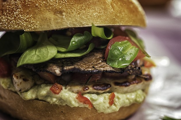 A portobello mushroom veggie burger on a hard roll with lettuce, tomato and sauce