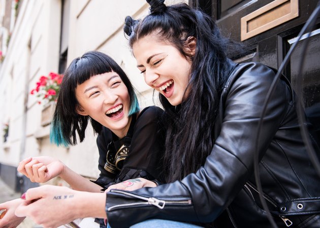 Two young stylish female friends sitting doorstep laughing