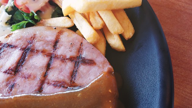 ham steak in white plate on wood table close up image.