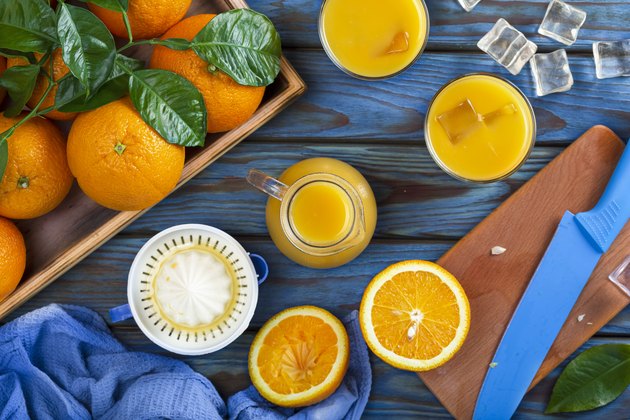 Orange juice in a glass, whole oranges, and sliced oranges on a blue wooden table.