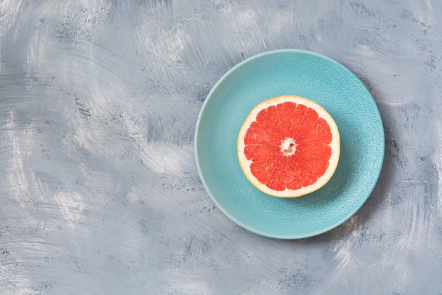 Half of the grapefruit is a blue plate, gray background. Copy space.