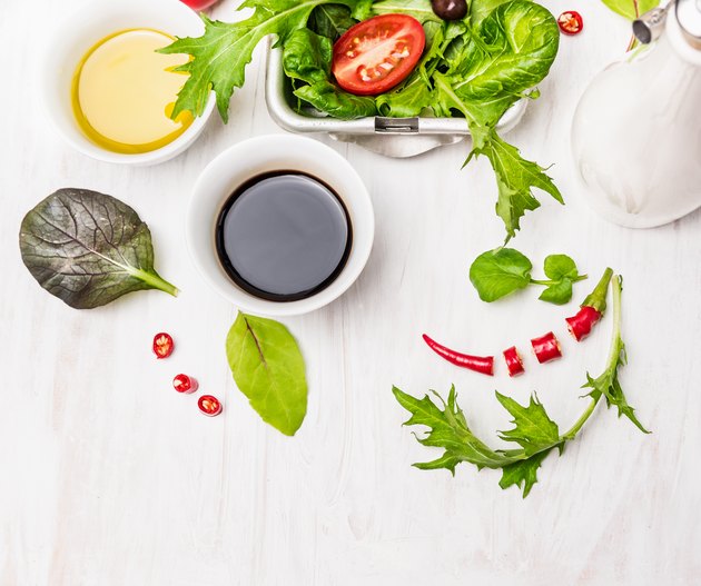 Salad preparation with oil and balsamic vinegar on white wooden