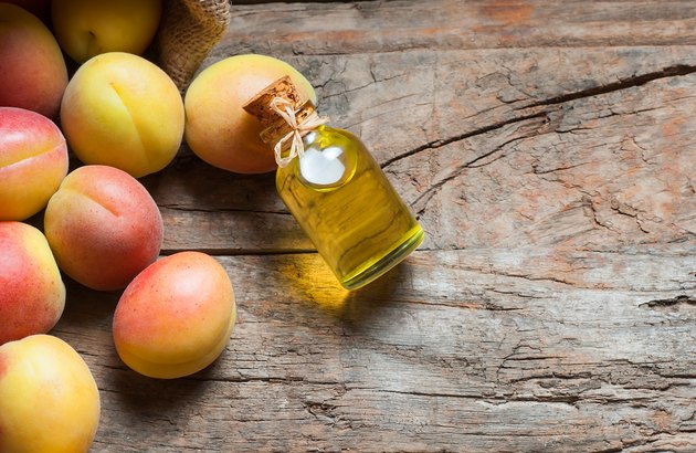 Glass bottle of Apricot seed kernel oil ( prunus armeniaca oleum ) with fresh ripe apricot fruits on wooden rustic background