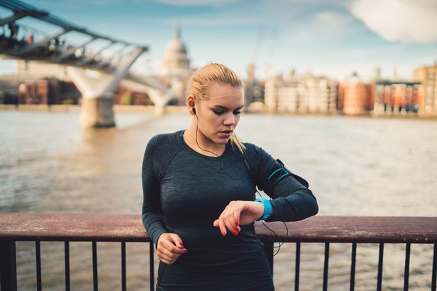 Sportswoman in UK checking pulse on smart watch during workout