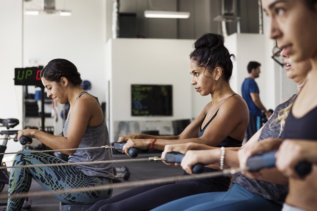 Determined female athletes exercising on rowing machines in crossfit gym to lose body fat