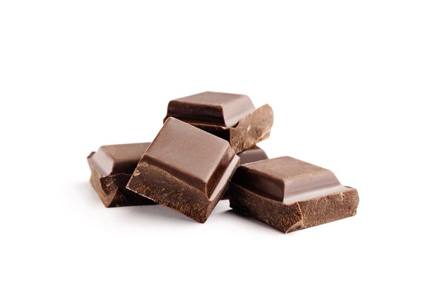 Pieces of bitter, dark chocolate bar, cubes on heap, isolated on white background, close-up view