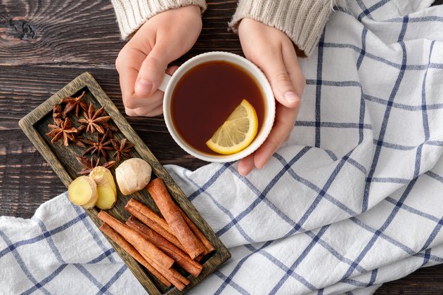 Female hands holding cup of tea with lemon on wooden table