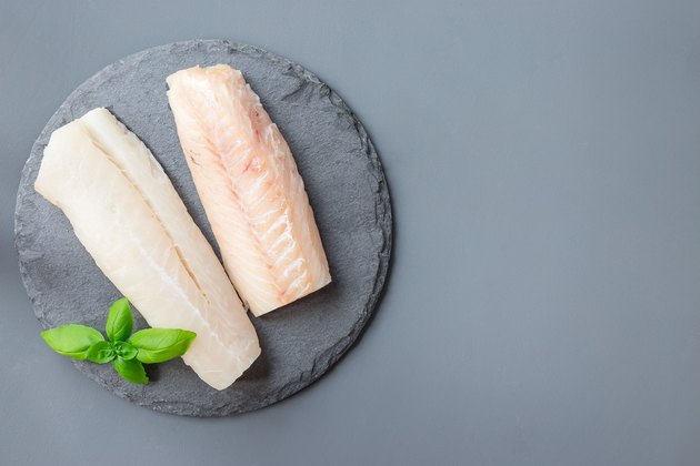 Fresh raw cod fillet with basil on stone plate, horizontal, copy space, top view