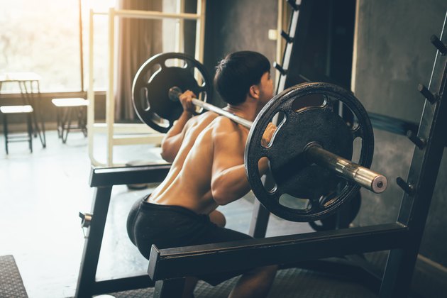 Athletic man performing barbell back squats at the gym.