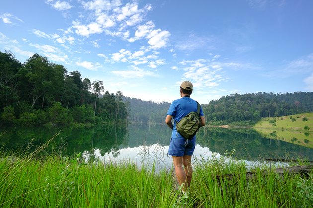 hiker in tall grass facing landscape of lake and forest