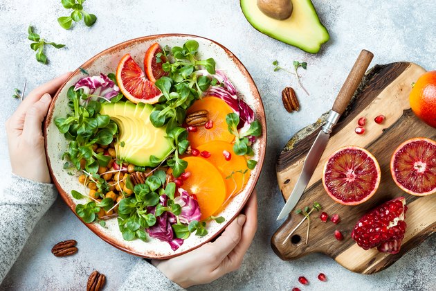 Vegan, detox Buddha bowl with turmeric roasted chickpeas, greens, avocado, persimmon, blood orange, nuts and pomegranate. Top view, flat lay