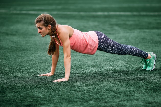 Woman in high plank position on grass completing a body-weight HIIT workout