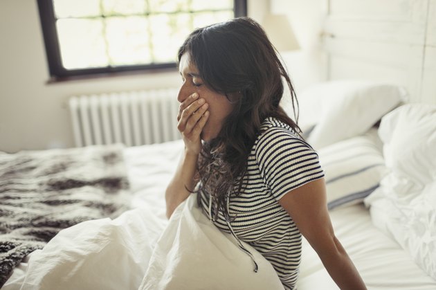 A young woman yawning as she sits up in bed in the morning