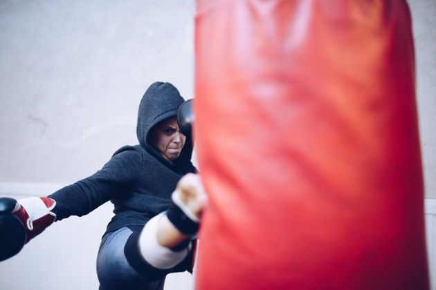 Young female kickboxer kicking punching bag at gym