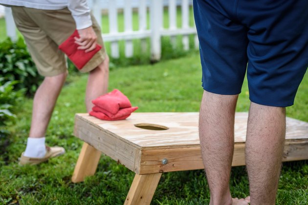 Young men playing cornhole game in backyard