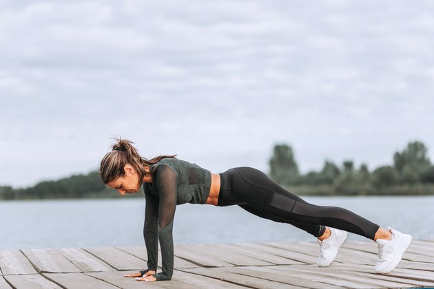 Side view of fit woman exercising on wooden river boardwalk.