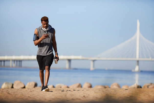 Serious black guy texting sms while walking over beach