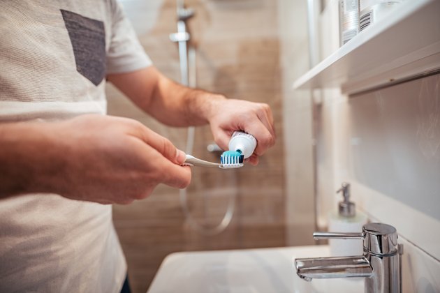 Close up of person pressant du dentifrice sur une brosse à dents au-dessus d'un évier
