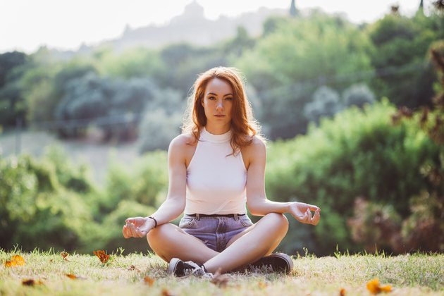 Italy, Verona, portrait of redheaded woman doing yoga exercise on a hill