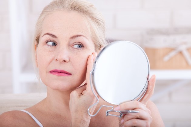 Forty years old woman looking at wrinkles in mirror. Plastic surgery and collagen injections. Makeup. Macro face. Selective focus