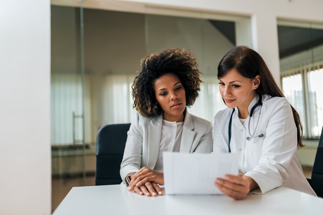 Portrait of a beautiful female doctor and patient looking at cholesterol test results.