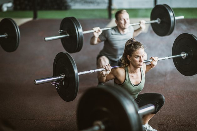 Young athletes exercising strength with barbells on cross training in a gym.