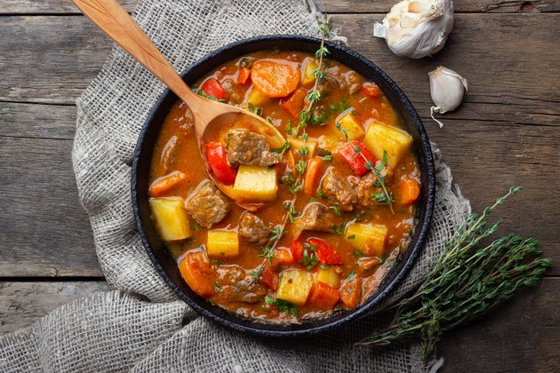 Goulash, beef stew or bogrash soup with meat, vegetables and spices in cast iron pan on wooden table.
