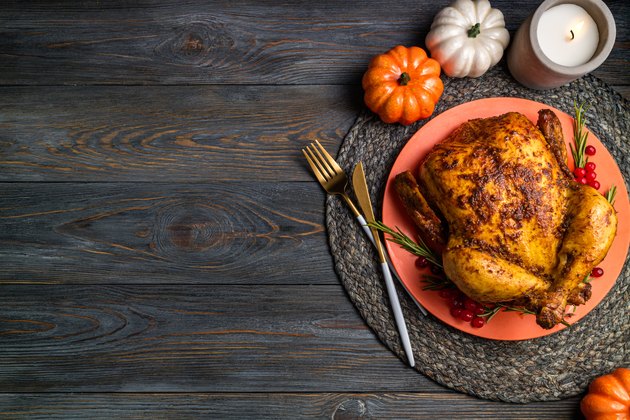 Baked turkey for Thanksgiving Day. Roasted whole chicken or turkey with herb rosemary and berries for thanksgiving dinner on wooden table. Festive table settings for Thanksgiving Day