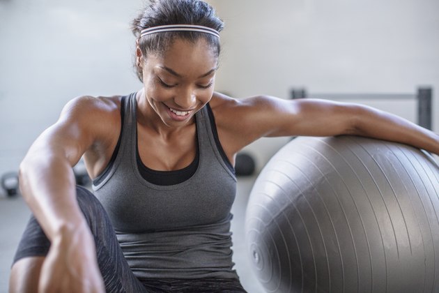 Smiling athlete looking down while exercising with medicine ball in gym