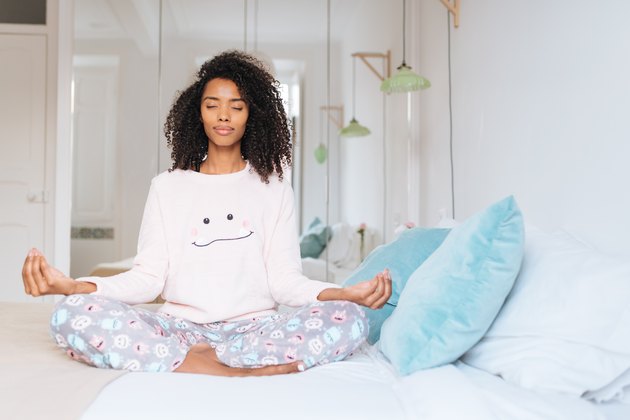Happy beautiful young black woman relaxed at home doing morning meditation in bed 'n