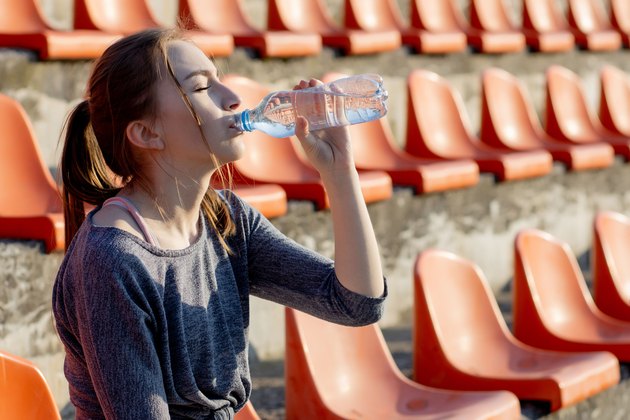 Young woman in sportswear relaxing after hard workout sit and drink water from special sport bottle after running on a stadium