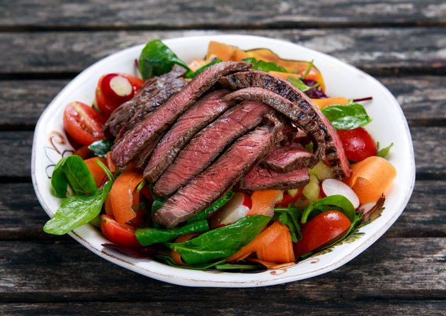 Slices of medium steak over a salad with mixed vegetables