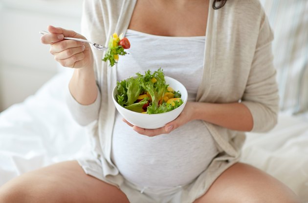 close up of pregnant woman eating salad at home