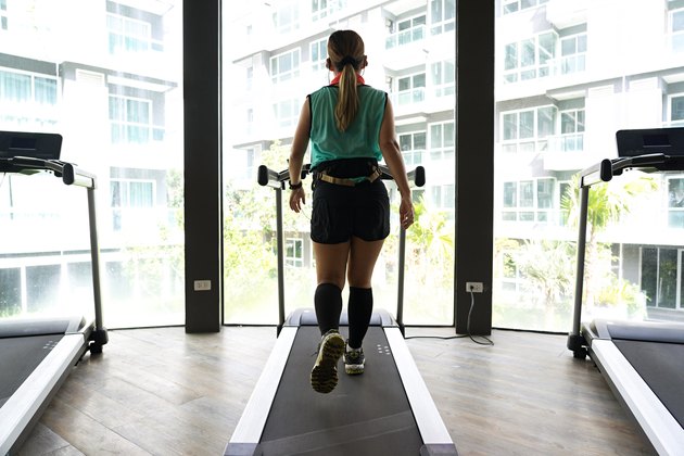 Asian woman walking on treadmill with bright buildings background