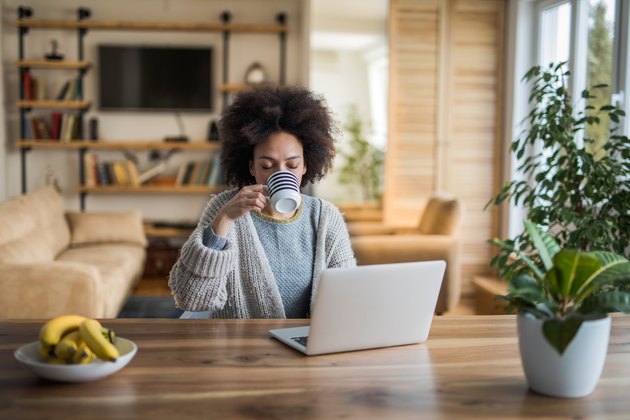 Young woman drinking coffee and using laptop at home
