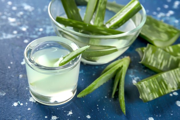 Glassware with fresh aloe vera juice and leaves on color table