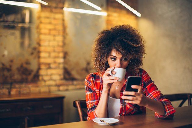 年轻女子在咖啡馆喝咖啡和使用手机