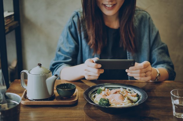 在咖啡馆，一名微笑的女子用智能手机拍下了桌上的饭菜