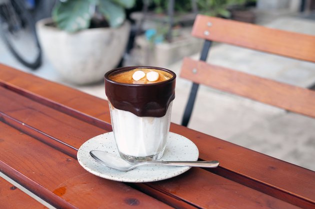 A glass of iced cocoa coffee latte; upper layer is black espresso shot lower is fresh milk decorated with melted black cocoa and marshmallow.