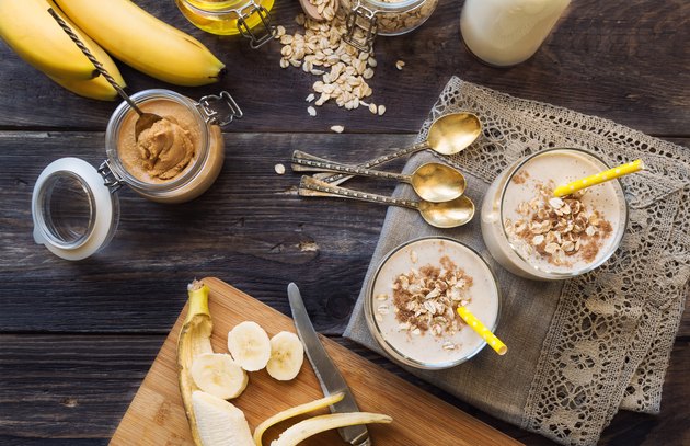 Fresh homemade nutritional smoothie with banana, oat flakes and peanut butter on rustic wooden background with ingredients.