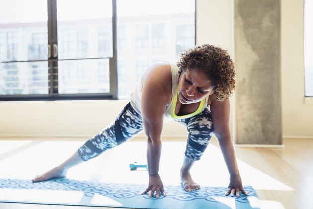Full length of woman practicing yoga on exercise mat against window in studio