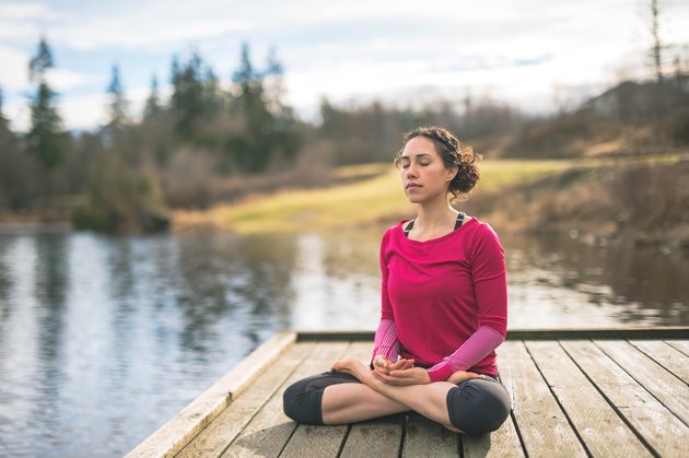 Young mom doing yoga outside by lake