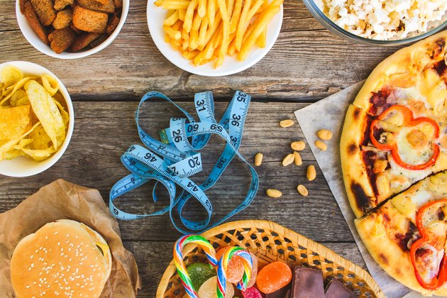 Fast food, tape measure on old wooden background. Concept of junk eating. Toned image. Top view.
