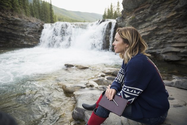 Pensive woman with journal at waterfall